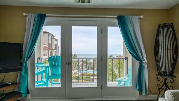 A room with a sliding glass door leading to a balcony with a pool and a view of buildings and the sea. - Villa Capriani 204B - Oceanfront - Pools - Hot Tubs - Restaurant (North Topsail Beach)