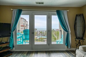 Una habitación con puerta de vidrio corredera que da a un balcón con piscina y vistas a edificios y al mar.