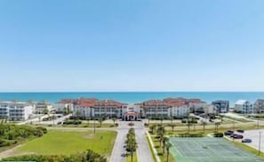 A coastal hotel with multiple buildings, a central entrance, and a tennis court.