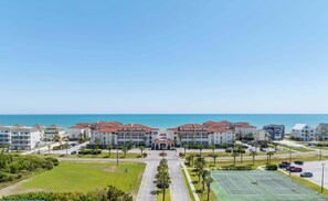 A multi-story hotel with a central courtyard, parking area, and a tennis court.