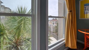 A room with a large window, a yellow curtain, and a view of buildings and palm trees outside. - Villa Capriani 204B - Oceanfront - Pools - Hot Tubs - Restaurant (North Topsail Beach)