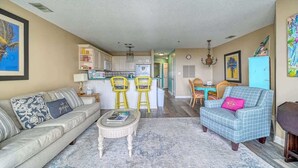 A living room with a sofa, chairs, a coffee table, and a dining area with a table and chairs. - Villa Capriani 204B - Oceanfront - Pools - Hot Tubs - Restaurant (North Topsail Beach)