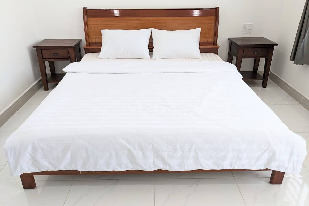 A neatly made bed with white linens, wooden headboard, and two bedside tables with drawers.