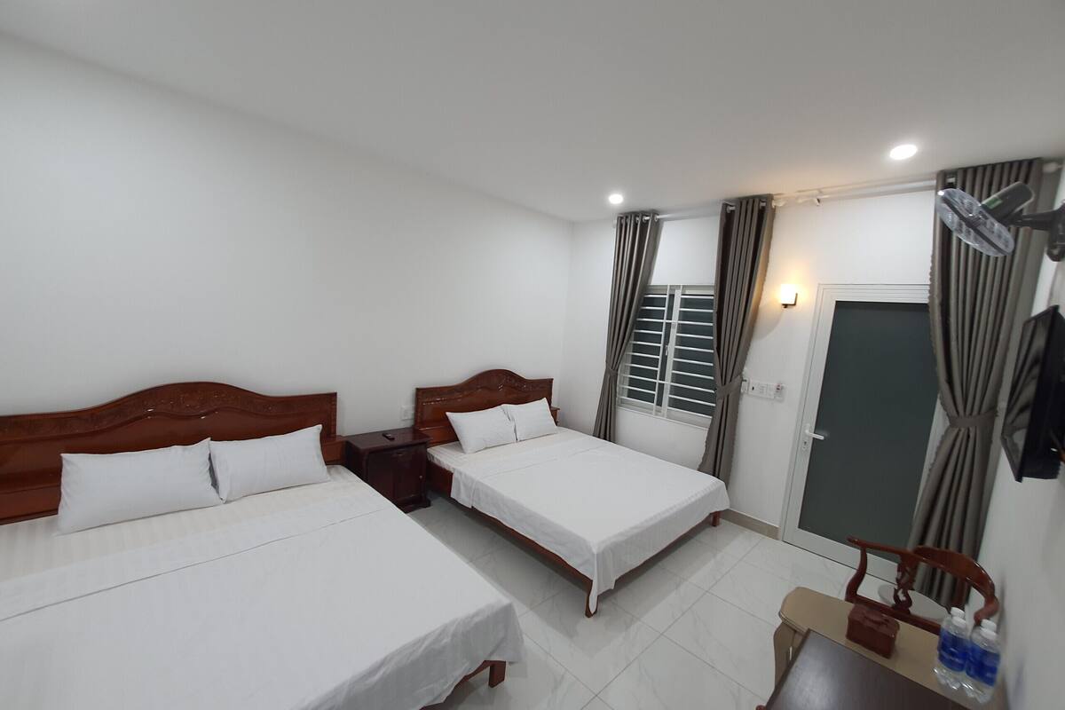 A hotel room with two beds, a desk, a chair, a window with curtains, and a door.