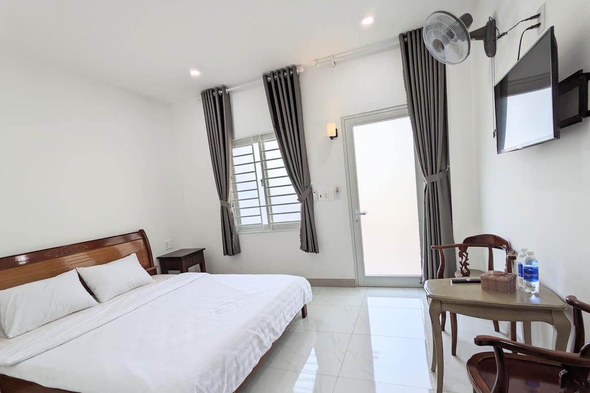 A hotel room with a bed, a desk with chairs, a television, and a window with curtains.