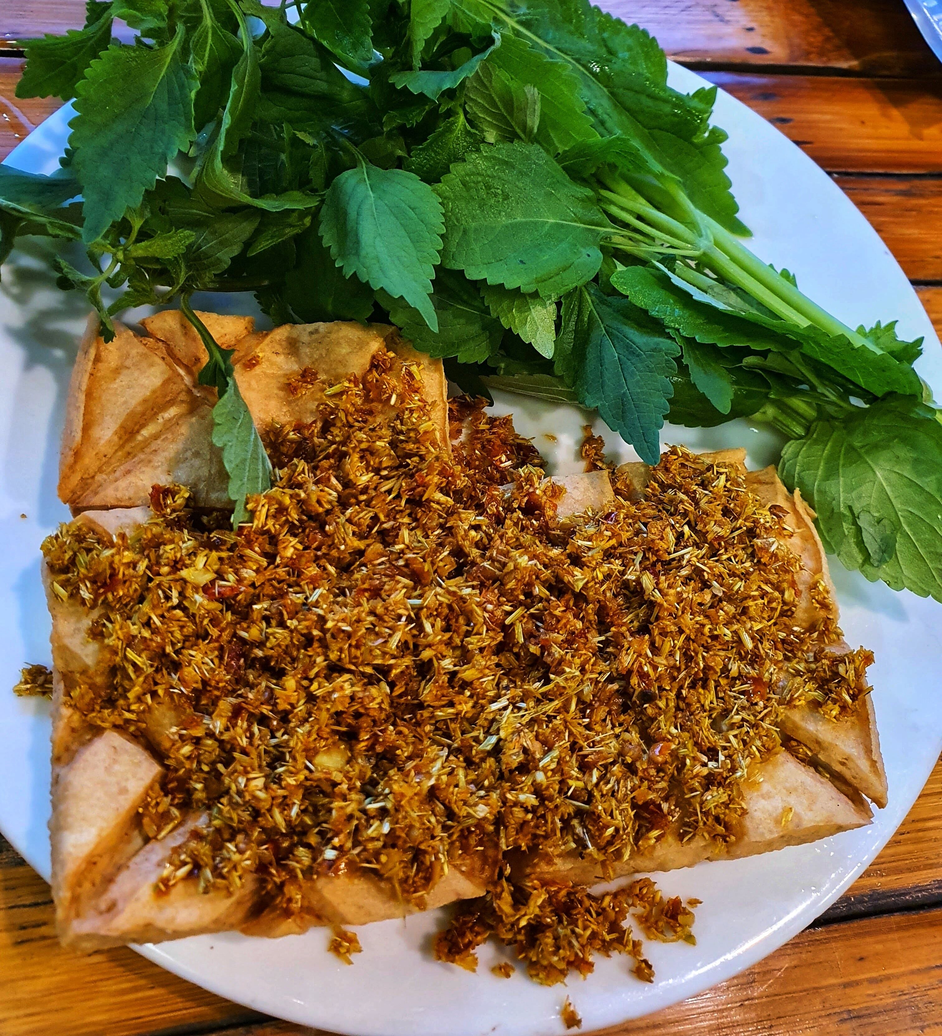 A plate with a dish topped with a fried mixture, accompanied by fresh herbs.