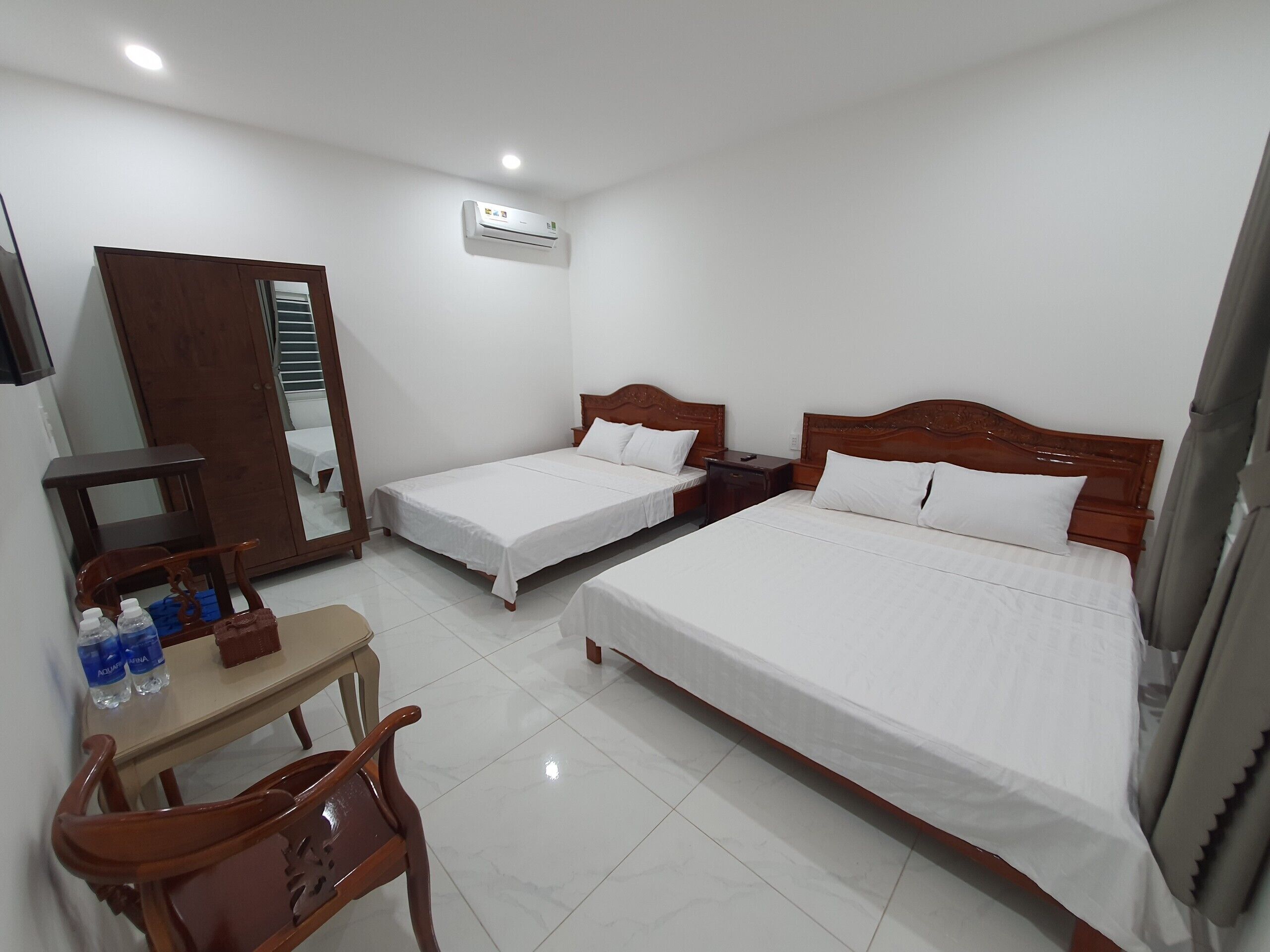 A hotel room with two single beds, a wooden desk, a chair, a wardrobe, and an air conditioning unit.