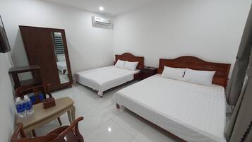 A hotel room with two single beds, a wooden desk, a chair, a wardrobe, and an air conditioning unit.