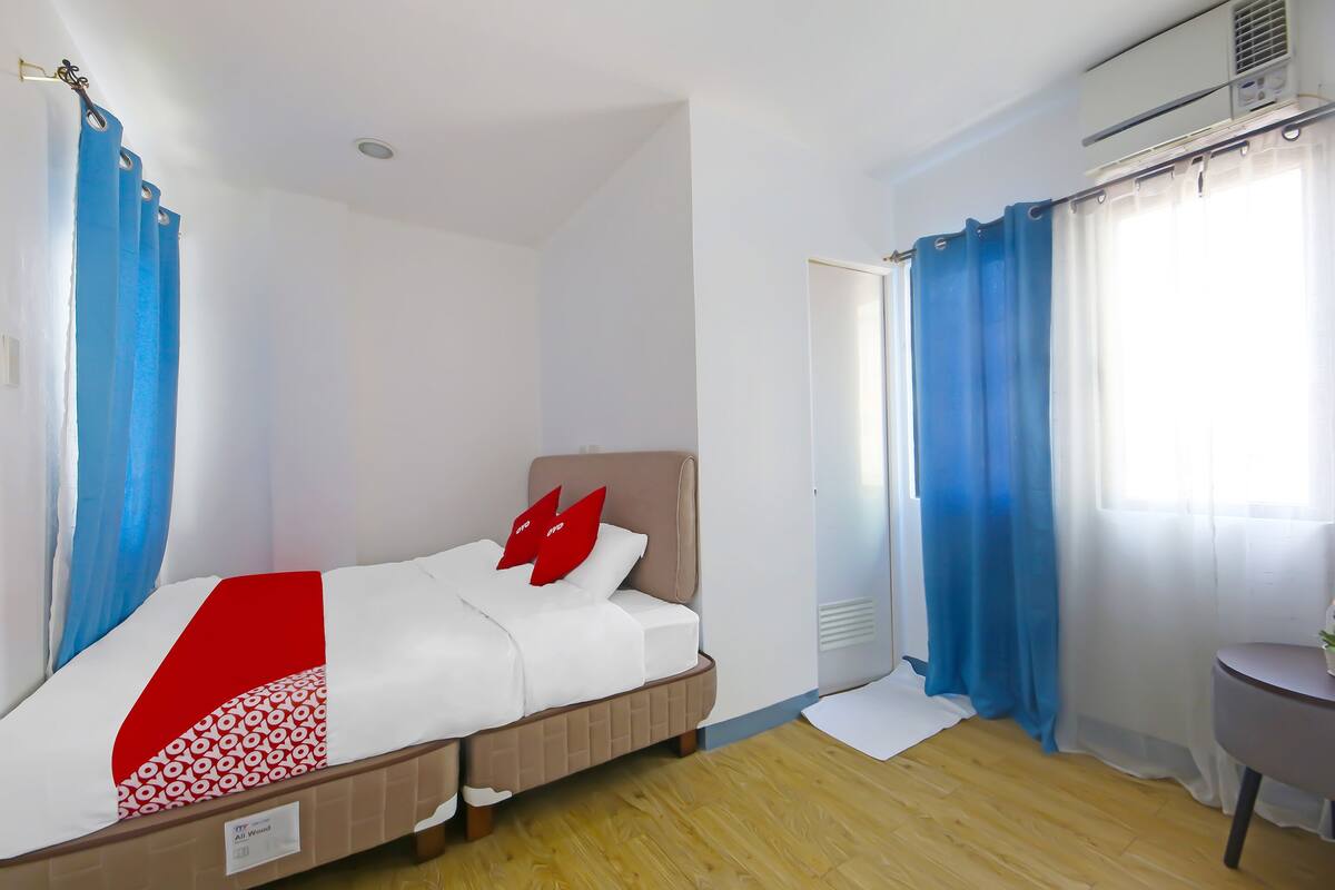 Hotellihuone, jossa on sänky, pieni pöytä ja ikkuna, jossa on verhot.