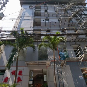 Um edifício de vários andares com escada de incêndio, palmeiras e uma placa com caracteres chineses.