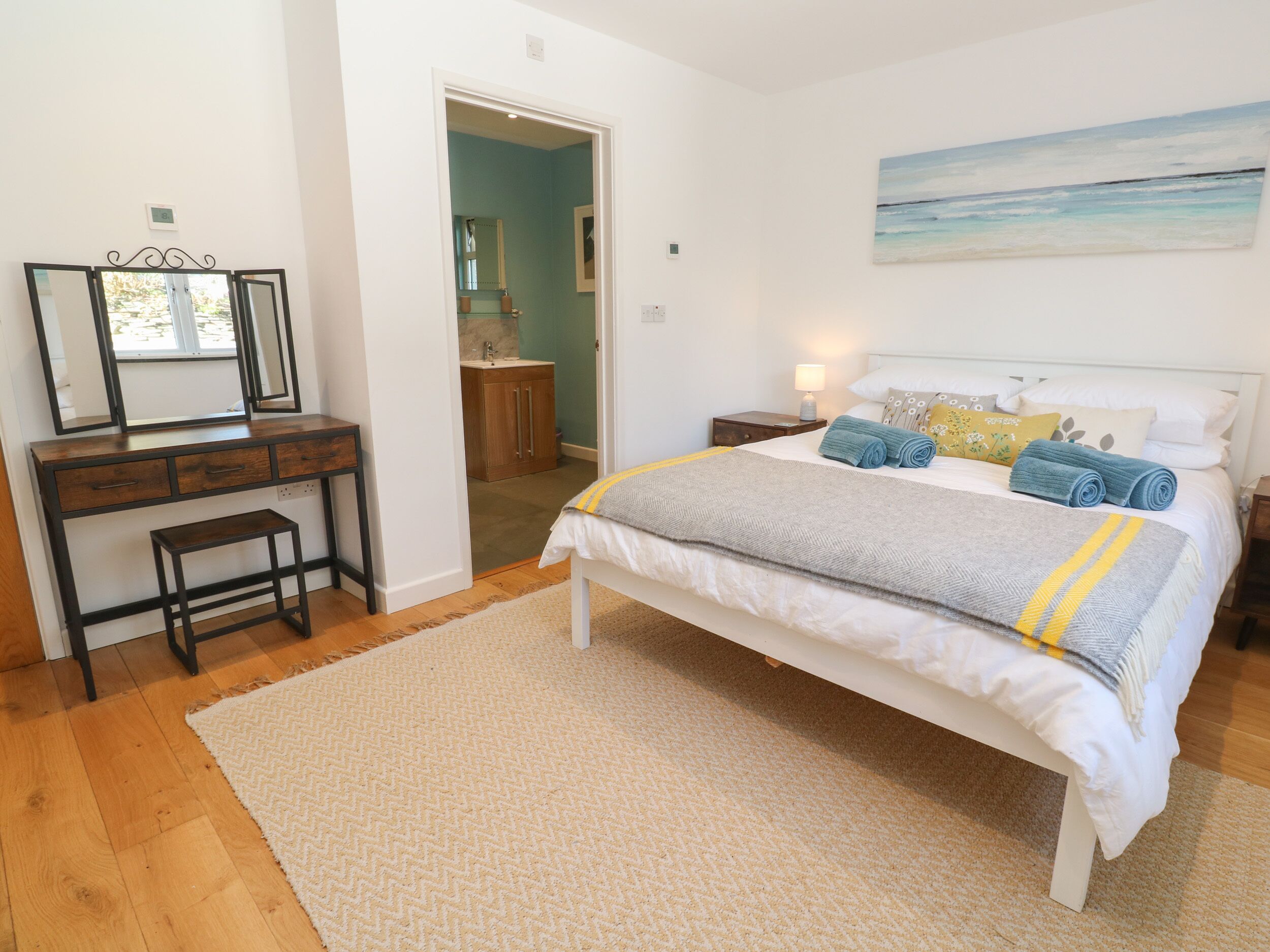 Un dormitorio con cama, mesitas de noche, cómoda, espejo y un cuadro en la pared.