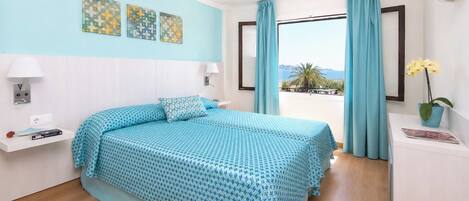 A bedroom with a bed, a nightstand, a lamp, a window with curtains, and artwork on the wall.