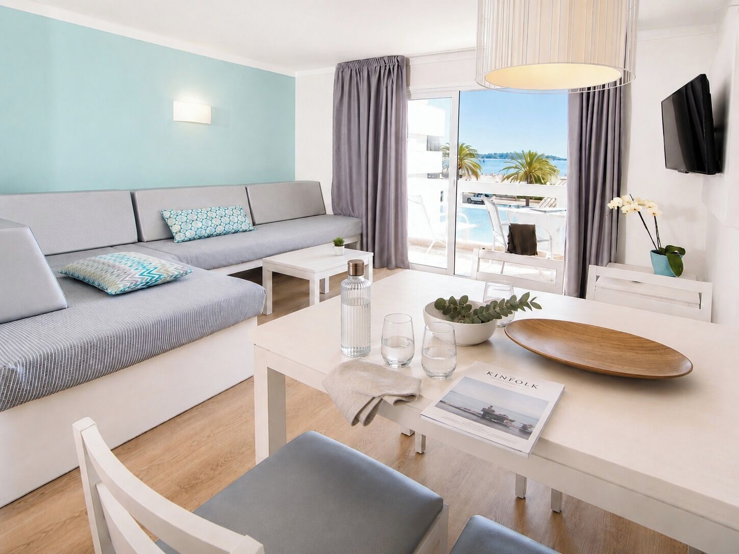 A modern hotel room with a sofa, dining table, and a view of the beach.