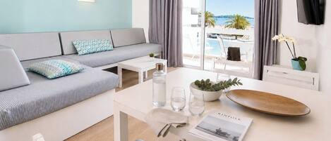 A modern hotel room with a sofa, dining table, and a view of the beach.