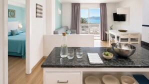 A modern kitchen with a marble countertop, a dining area with a table and chairs, and a bedroom with a bed and a view of the sea. - Apartamentos Sivella (Pollenca)