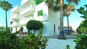 A white building with balconies and green shutters, surrounded by palm trees and a gravel courtyard. - Apartamentos Sivella (Pollenca)