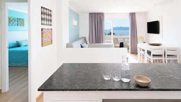 Una cocina moderna con encimera de mármol, zona de comedor con mesa y sillas blancas, y vistas al mar a través de amplios ventanales.