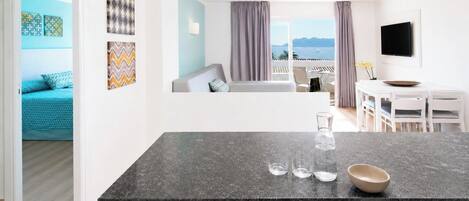 A modern kitchen with a marble countertop, a dining area with a white table and chairs, and a view of the sea through large windows.