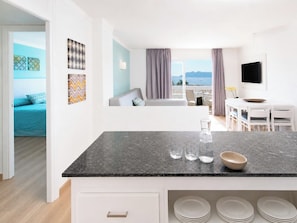 A modern kitchen with a marble countertop, a dining area with a white table and chairs, and a view of the sea through large windows.