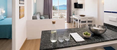 A modern kitchen with a marble countertop, a dining area with a table and chairs, and a bedroom with a bed and a view of the sea.