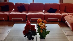 Ett vardagsrum med en röd soffa, ett soffbord med blommor och ett stort fönster med utsikt över ett snötäckt landskap.