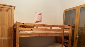 En våningssäng med en träram, ett litet skåp och en dörr med ett glasparti.