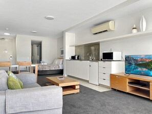 Moderni olohuone, jossa on sohva, sohvapöytä, televisio ja pieni keittiö.
