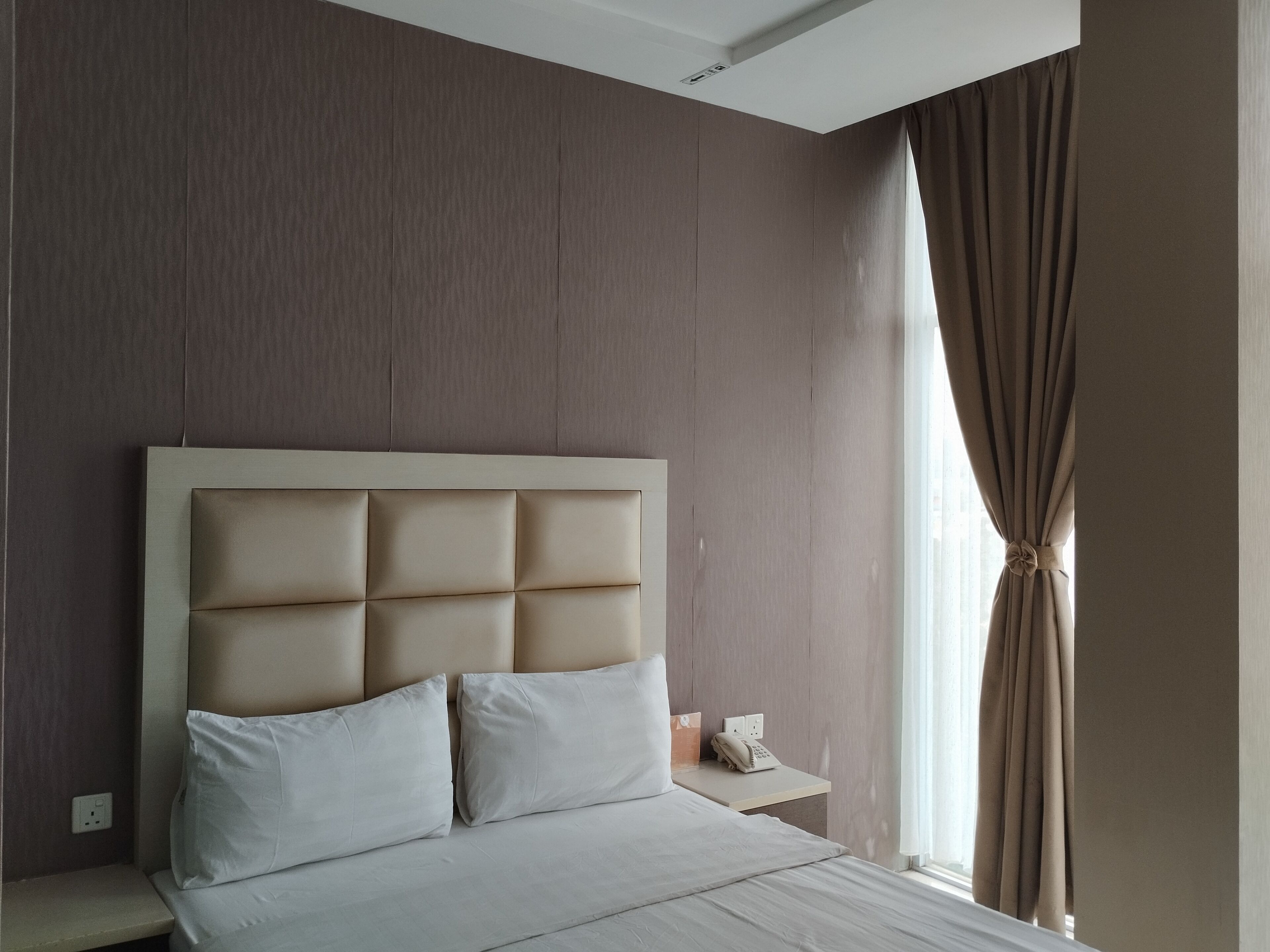 A modern hotel room with a large bed, a bedside table, and a window with curtains.