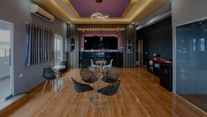 A modern interior with a dining area featuring a central table and chairs, a kitchen area with a bar, and a large window providing natural light. - osaka hotel batam (Batam)