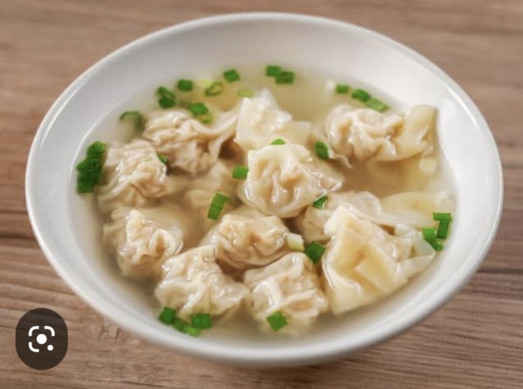 A bowl of soup with dumplings and chopped green onions.