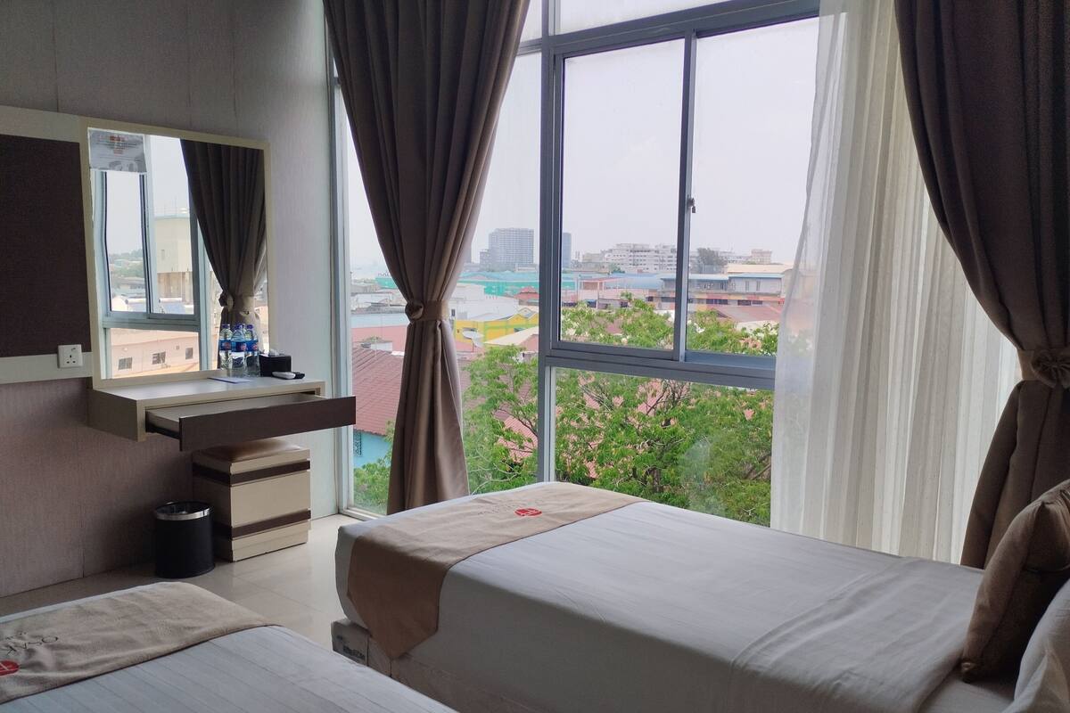 A hotel room with two beds, a desk, a mirror, and a window with curtains.