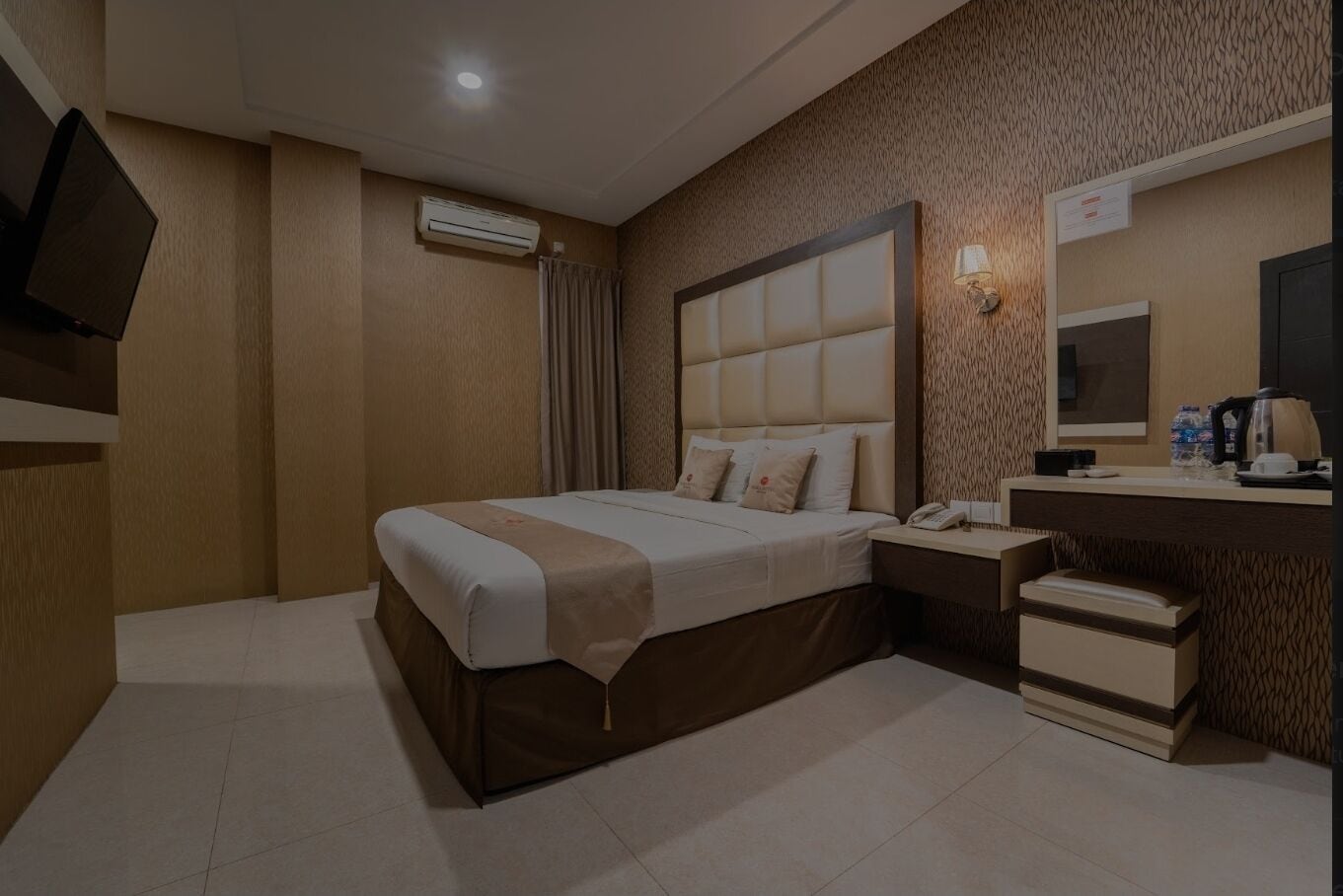 A hotel room with a large bed, a bedside table, a desk, a chair, an air conditioning unit, a mirror, and a television.