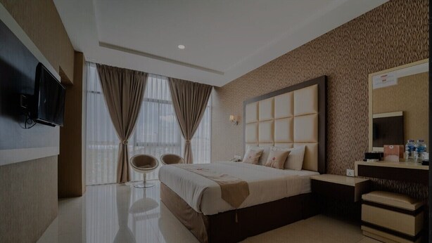 A modern hotel room with a large bed, a bedside table, a mirror, and a seating area with two chairs. - osaka hotel batam (Batam)