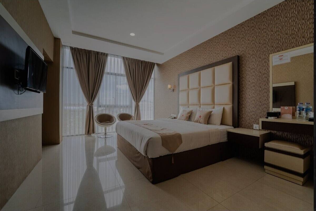 A modern hotel room with a large bed, a bedside table, a mirror, and a seating area with two chairs.
