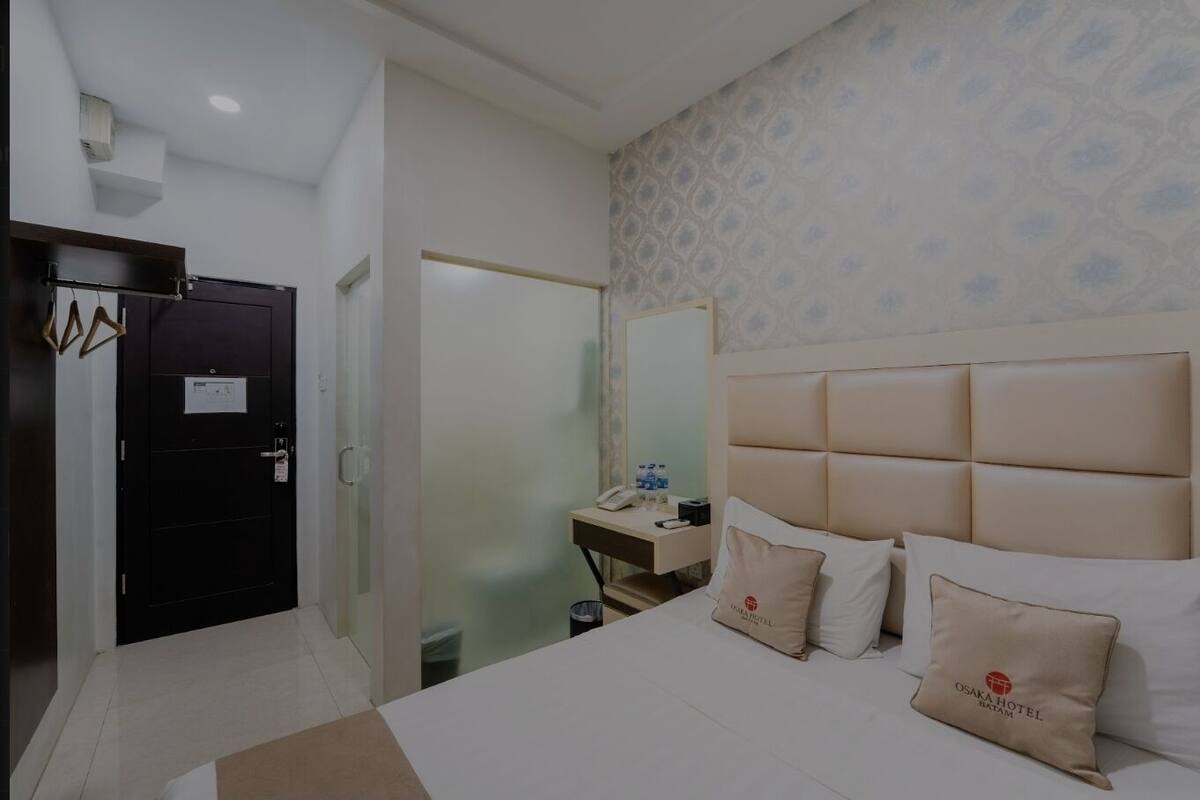 A hotel room with a large bed, a bedside table with a phone and water bottle, a mirror, and a door with a sign.