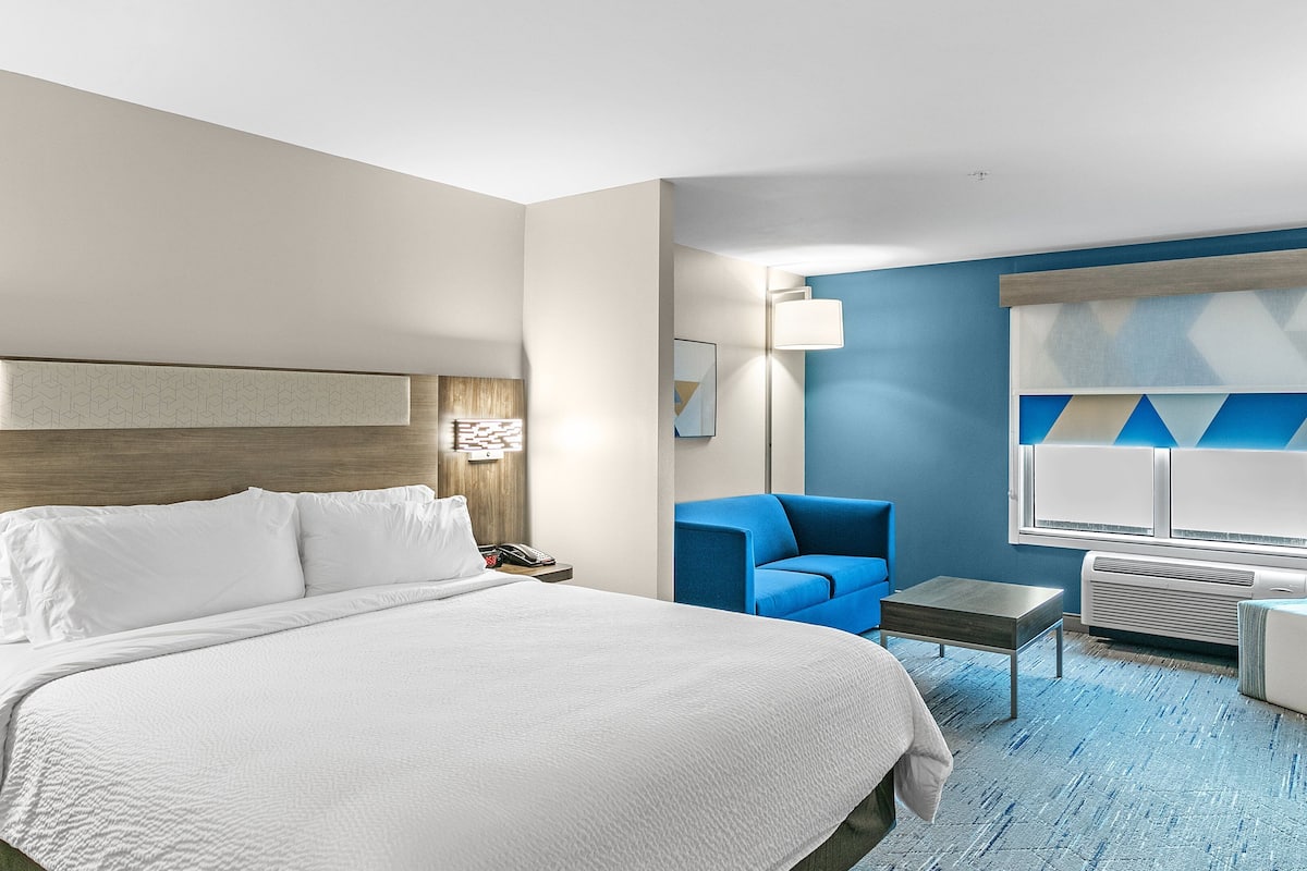 Ein Hotelzimmer mit einem großen Bett, einem blauen Sessel, einem kleinen Tisch und einem Schreibtisch.