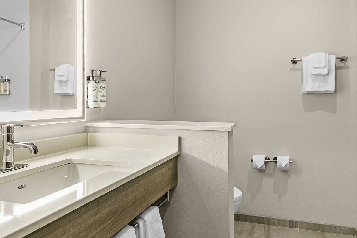 Ein Badezimmer mit Waschbecken, Spiegel, Handtuchhalter, Toilette und Duschbereich.