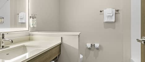 Ein Badezimmer mit Waschbecken, Spiegel, Handtuchhalter, Toilette und Duschbereich.