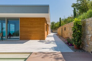 A modern house with a wooden facade, a stone wall, and a garden with potted plants. - Stunning views, an infinity pool, privacy, and nature. Villa (Brenzone sul Garda)