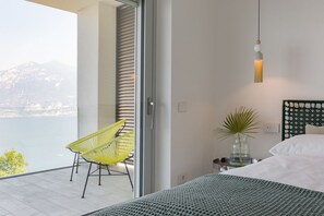 A modern bedroom with a bed, a nightstand, a vase with a plant, and a view of the outdoors. - Stunning views, an infinity pool, privacy, and nature. Villa (Brenzone sul Garda)
