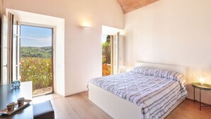 Ein Schlafzimmer mit einem Bett, einem Tisch mit Tassen und Blick auf Grün hinter dem Fenster.