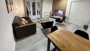A modern living room with a sofa, a dining table, a TV, and a piano. - LeRelaisdOdile * Spacious & Bright Apartment * (Cambrai)