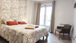 A bedroom with a bed, a chair, a TV, and a window with curtains. - LeRelaisdOdile * Spacious & Bright Apartment * (Cambrai)