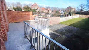 A balcony with a metal railing, a brick wall, and a grassy area in the background. - LeRelaisdOdile * Spacious & Bright Apartment * (Cambrai)