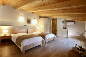 A bedroom with two beds, wooden ceiling beams, a nightstand, a lamp, a chair, and a small table with a vase. - GK Mediterranean Village -AirportShuttle by GK Hospitality Group (Markopoulo Mesogaias)