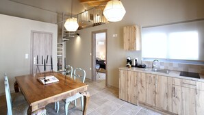 A modern kitchen with wooden cabinets, a dining table, and hanging pendant lights. - GK Mediterranean Village -AirportShuttle by GK Hospitality Group (Markopoulo Mesogaias)
