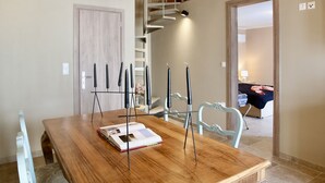 A dining area with a wooden table, chairs, and a staircase leading to an upper level. - GK Mediterranean Village -AirportShuttle by GK Hospitality Group (Markopoulo Mesogaias)