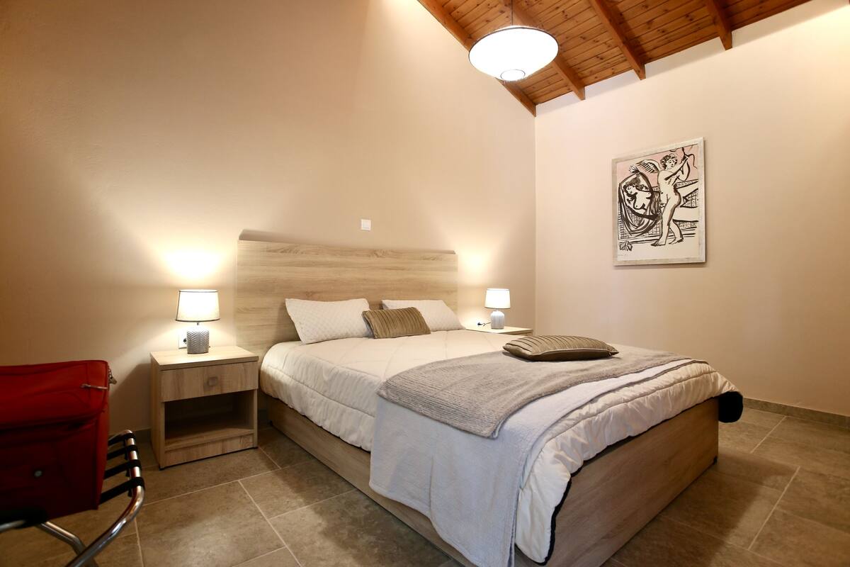 A bedroom with a bed, bedside lamps, a red chair, and a wall art piece.