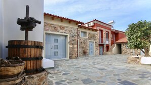 A courtyard with stone flooring, a wooden barrel, and a metal water pump. - GK Mediterranean Village -AirportShuttle by GK Hospitality Group (Markopoulo Mesogaias)