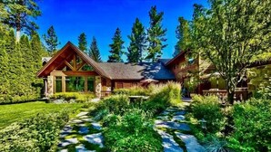A log cabin with a sloped roof, surrounded by dense greenery and tall trees. - Lakefront Legacy luxury Lake Tahoe Estate Camp Richardson luxe01 (South Lake Tahoe)